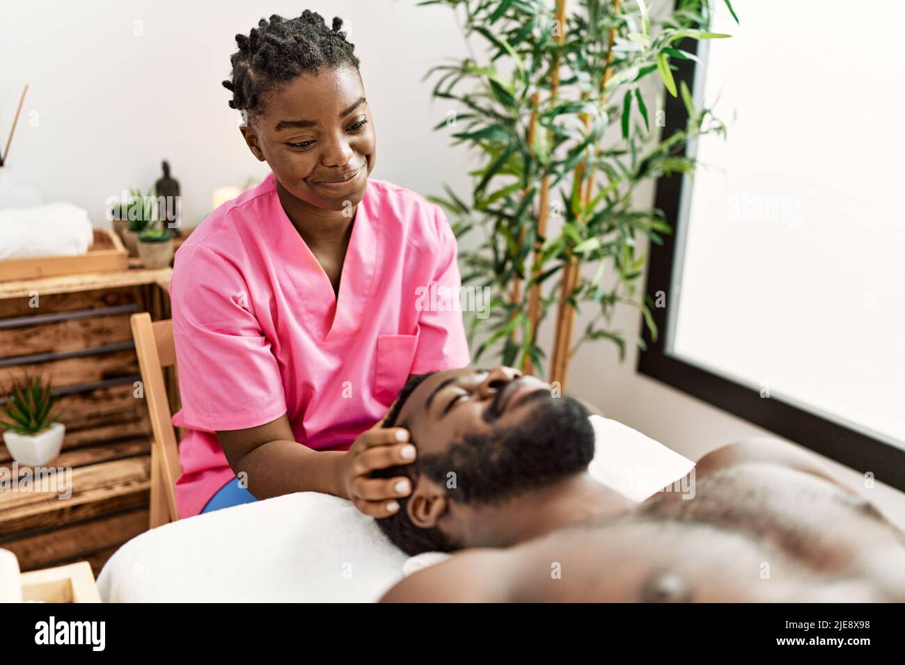 Young physiotherapist woman giving head massage to african american man at the clinic. Stock Photo
