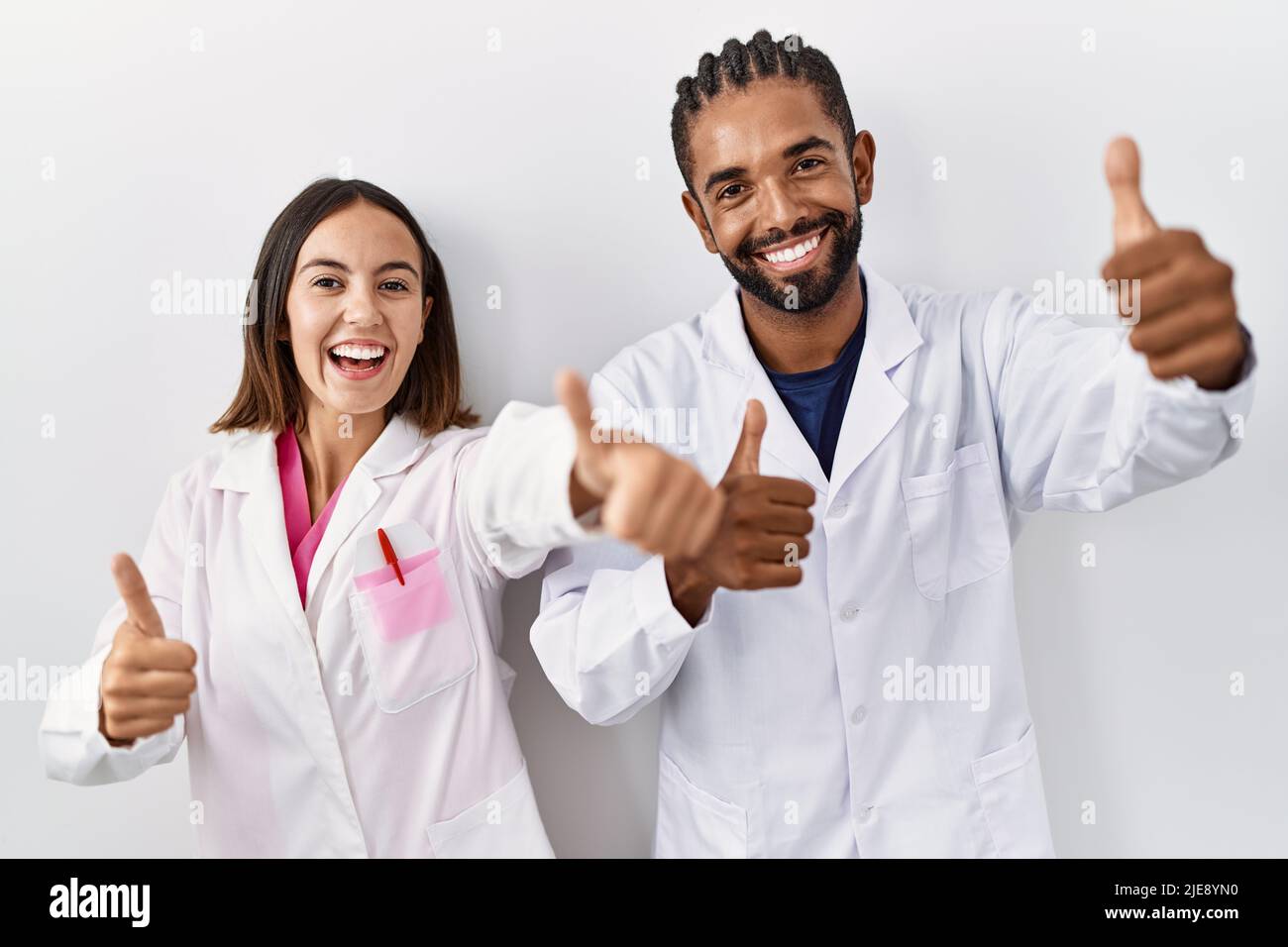 Young hispanic doctors standing over white background approving doing ...