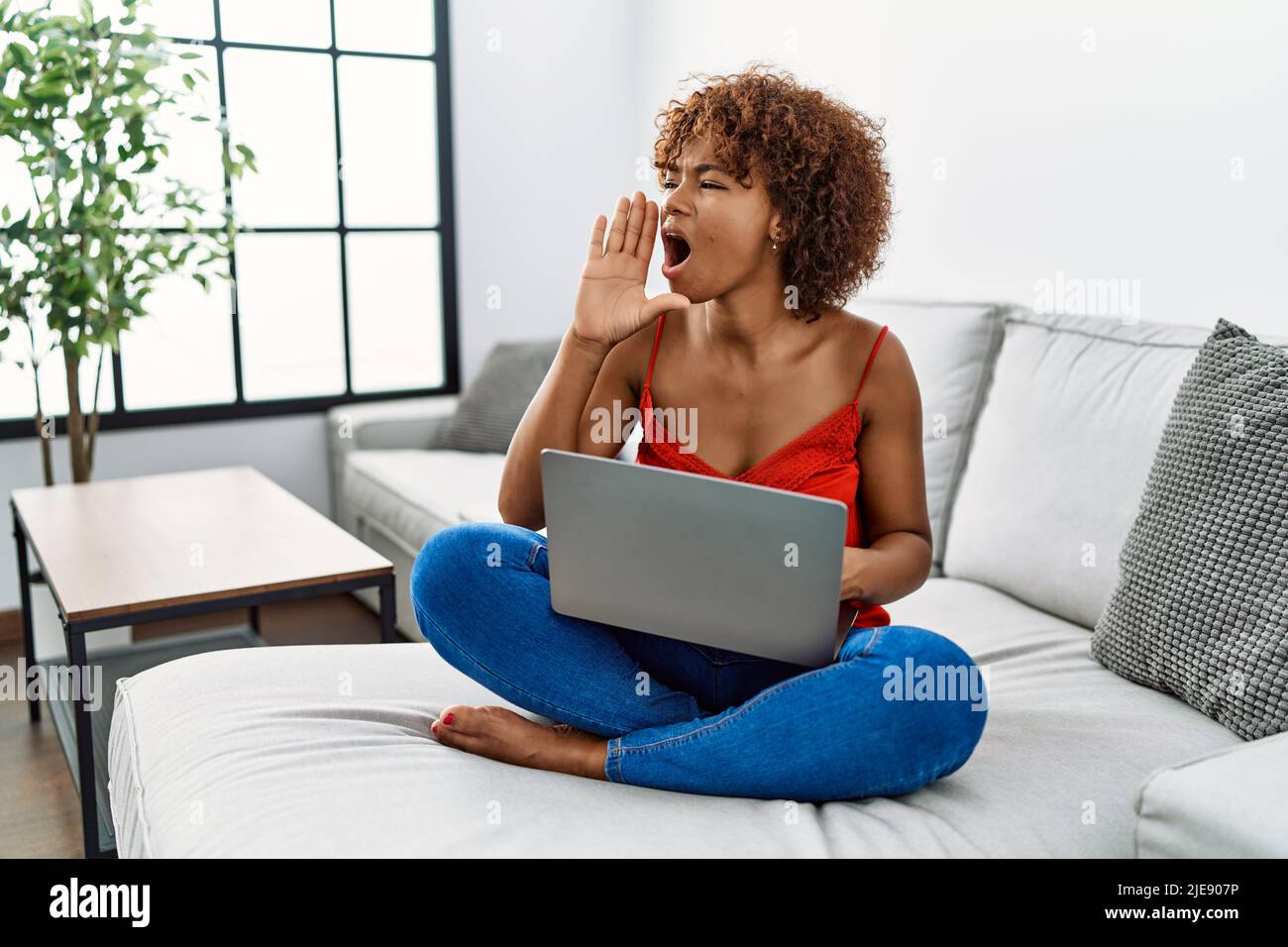 Young african american woman sitting on the sofa at home using laptop ...