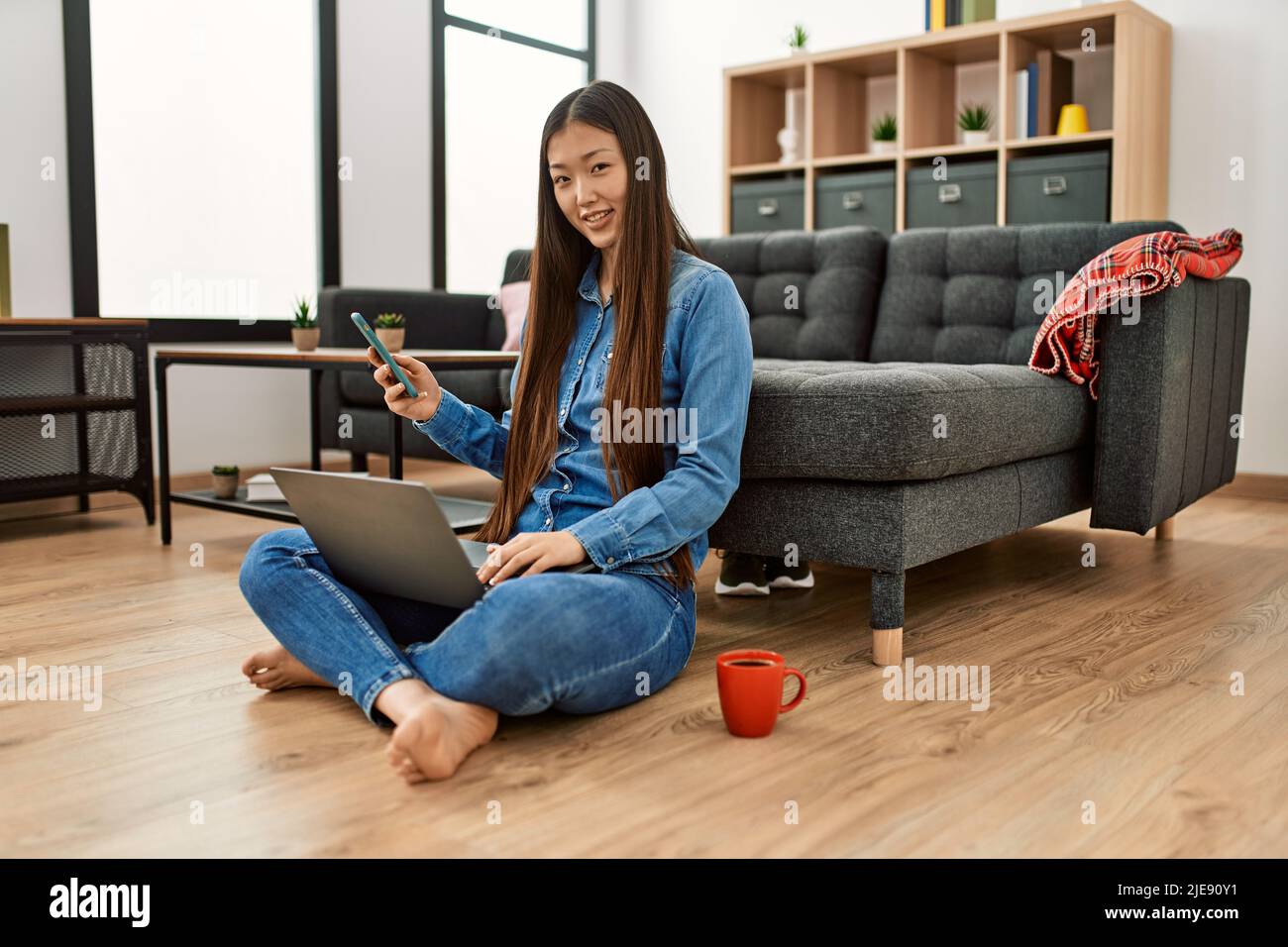 Young chinese girl using laptop and smartphone sitting on the floor at ...