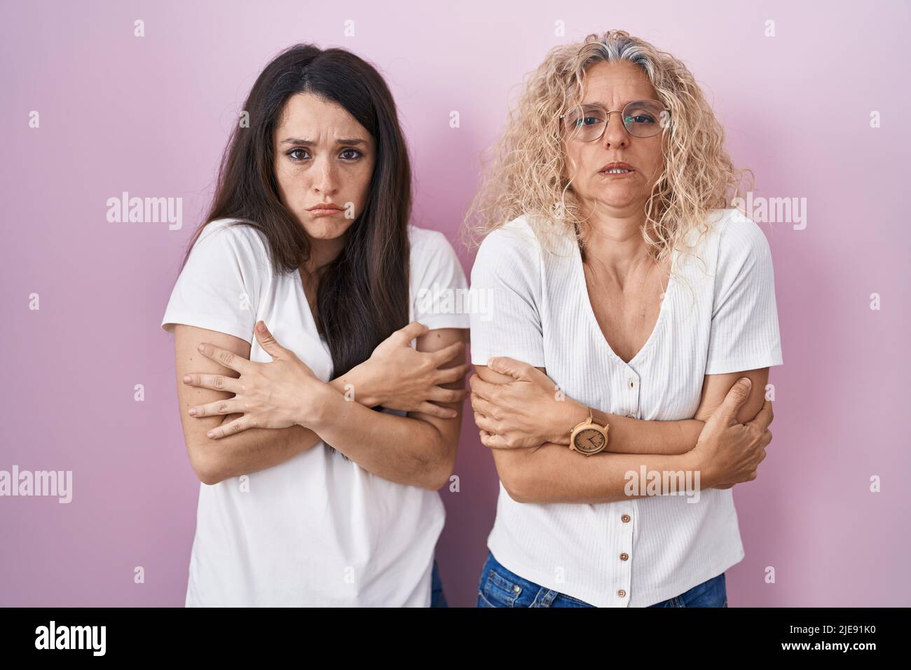 Mother And Daughter Standing Together Over Pink Background Shaking And