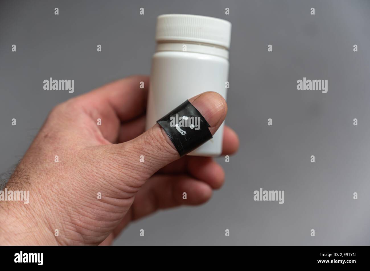 Middle-aged man holds white medicine or vitamin vial in his hand. Phalanx his thumb wrapped around black electrical tape. Happy, smiling face is paint Stock Photo