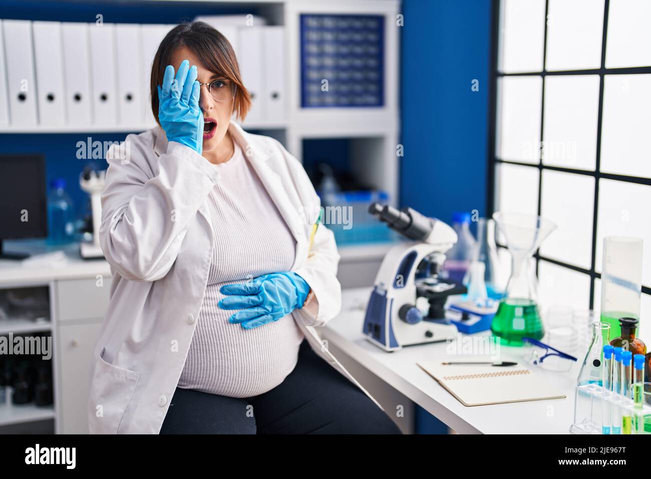 Pregnant woman working at scientist laboratory yawning tired covering