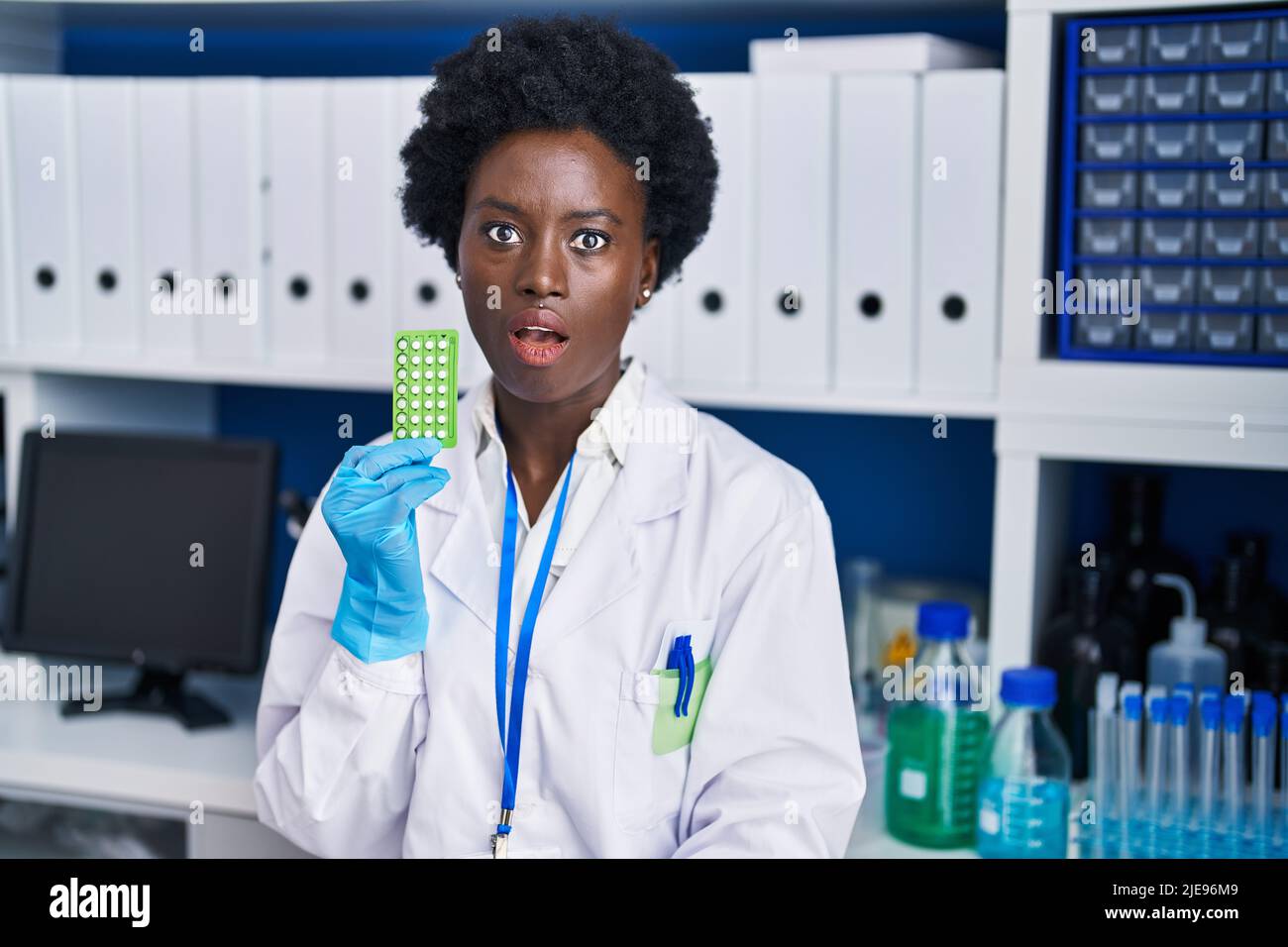 African Young Woman Working At Scientist Laboratory Holding Birth Control Pills Scared And 