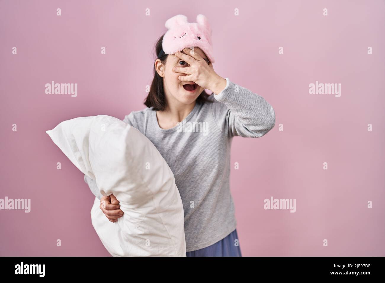 Woman with down syndrome wearing sleeping mask hugging pillow peeking