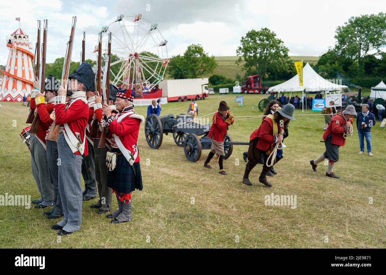 Members of the 4th King's Own Regiment of Foot (left) parade as members of the Devereaux's Regiment pull a gun towards the arena during the Chalke Valley History festival at Broad Chalke, Near Salisbury, Wiltshire. Picture date: Sunday June 26, 2022. Stock Photo