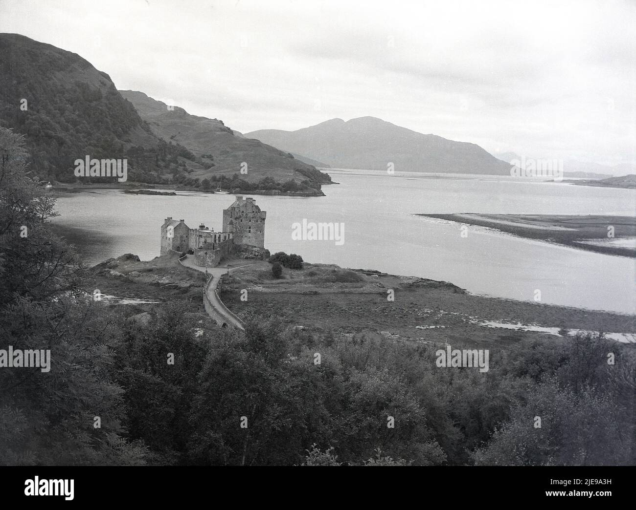 1950s, historical view from this era of Eilean Donan castle and surrounding landscape with highland and lochs, Scottish highlands, Scotland, UK.  First built in the 13th century, the castle was destroyed in 1719 when a Spanish fleet arrived to support the Jacobite uprising. It was rebuilt between 1919 and 1932 by Lt Co. John MacRae-Gilstrap, a relative of the Clan MacRae, original constables of the MacKenzies of Kintail, owners of the castle and surrounding lands. It was opened to the public in 1955. Stock Photo