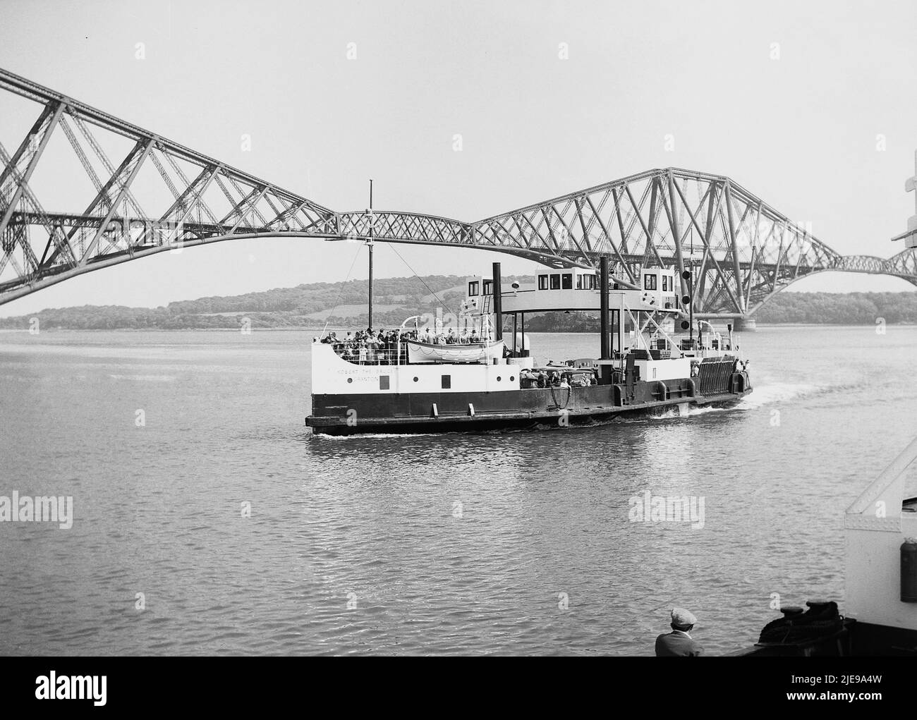 1956, historical view from this era of the Robert The Bruce ferry on the water beside the Forth Bridge, the world's first major steel structure. A cantilever railway bridge across the Firth of Forth in East of Scotland, near Edinburgh, its opening in 1890 was a major milstone in modern railway civil engineering and is the world's longest cantilever bridge. The ferry, Robert The Bruce, was built in 1934 by Clyde shipbuilders, William Denny, and could carry 500 passengers and 28 cars. It stopped operating in 1964 when the Forth Road Bridge opened. Stock Photo