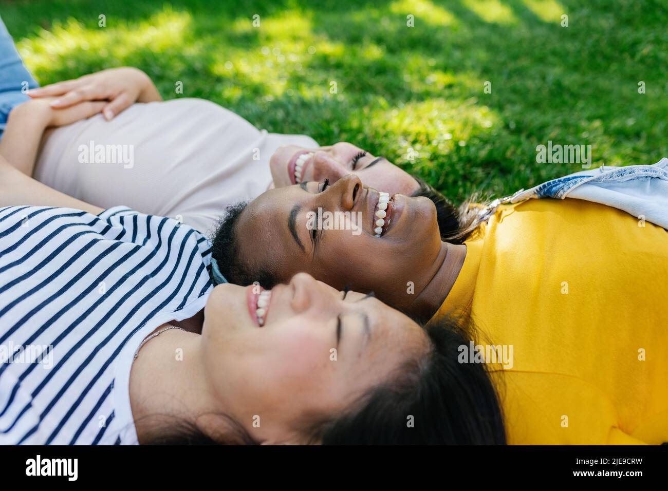 Three multiracial young women friends laughing together outdoors Stock Photo