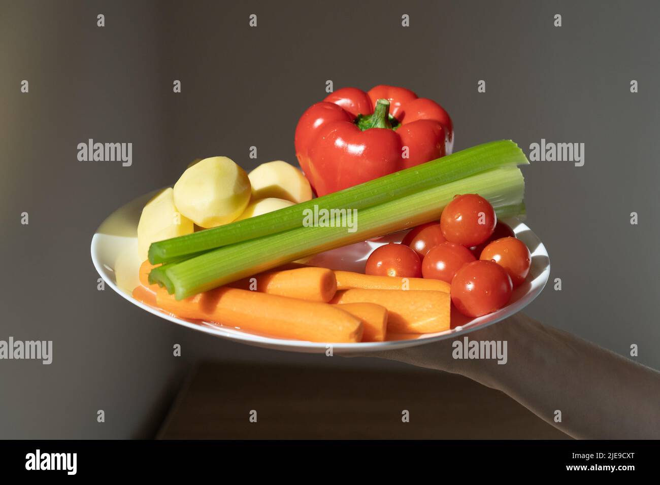 Hand holds plate with cherry tomatoes, carrots, celery, peppers and potatoes in rays of sunlight.  Stock Photo