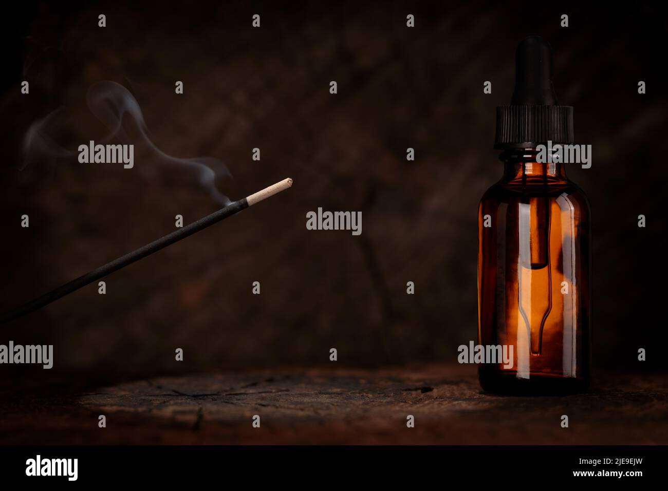 Mockup for relaxing oil. Lit incense on a rustic dark wood background. Spiritual ambiance, bottle with dropper. Stock Photo