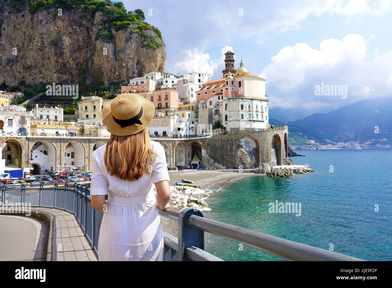 Italian Beauty Scenery. Back view of young woman with straw hat and white dress walking to Atrani village, Amalfi Coast, Italy. Stock Photo