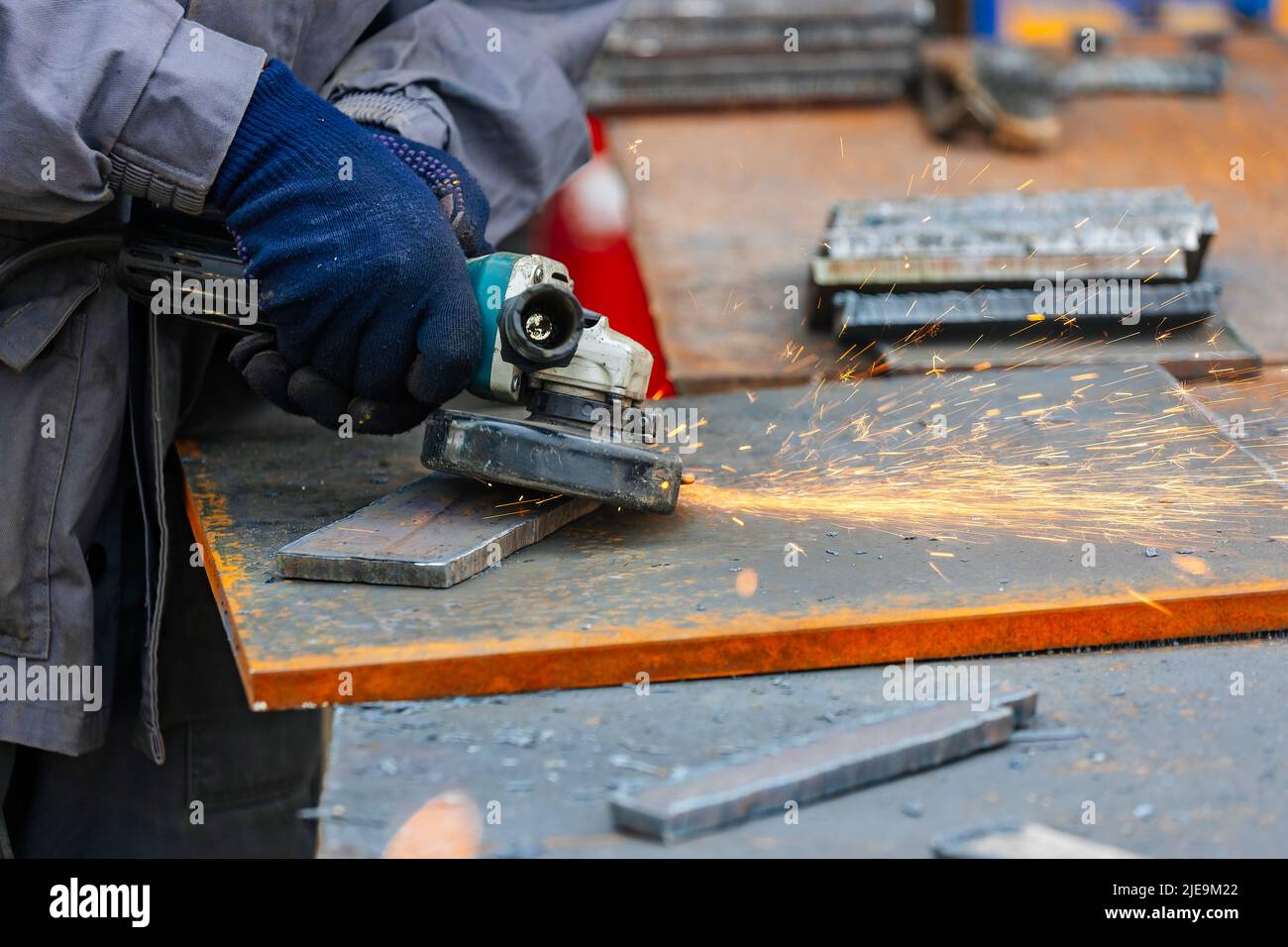 Worker on workbench grinds sheets of metal with grinder and sparks fly. Hands with close-up instrument. Authentic scene workflow. Processing of iron blanks for construction. Stock Photo
