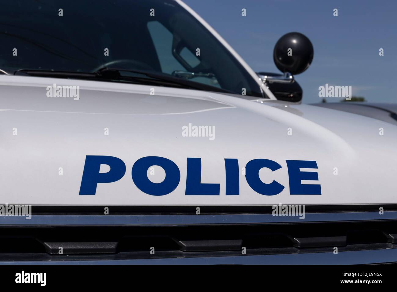 POLICE printed on the front of a police car in blue text and a spotlight in the background. Stock Photo