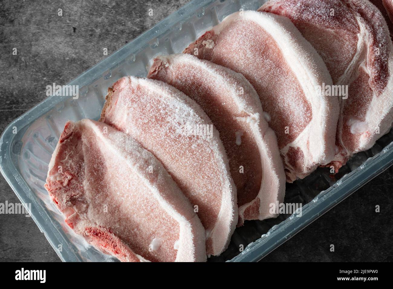 Frozen pork chops in plastic tray packaging thawing. On a concrete