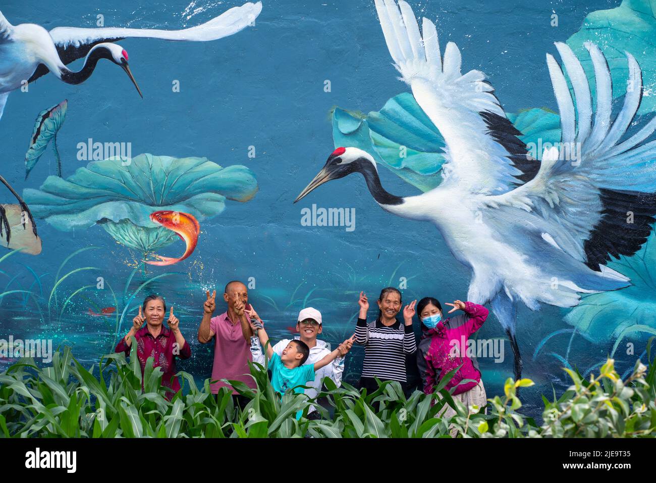 (220626) -- LIJIANG, June 26, 2022 (Xinhua) -- Liu Zhicheng (C) poses for a photo with villagers after finishing a wall painting in Yongsheng County, Lijiang City, southwest China's Yunnan Province, June 24, 2022. A non-profit 'post-95s' wall painter, hailing from Yongsheng County of Lijiang City, gained popularity both among villagers in his hometown and netizens on social media platforms. The mural artist named Liu Zhicheng has painted more than 20 wall paintings of different themes in many villages of his hometown. His artworks have added color to the villages and attracted many touri Stock Photo