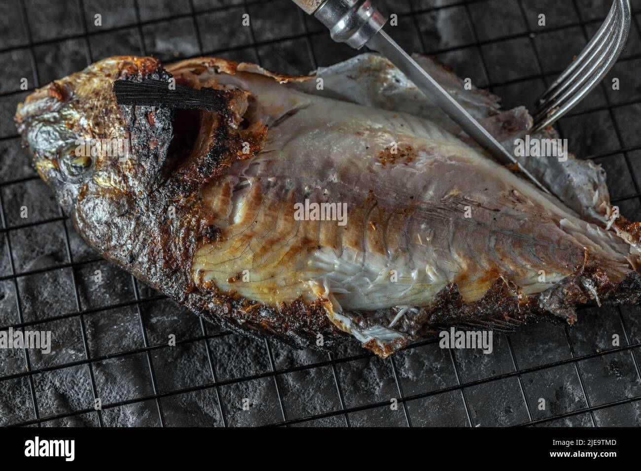 Eating whole grilled Dorado or Sea Bream on dark textured