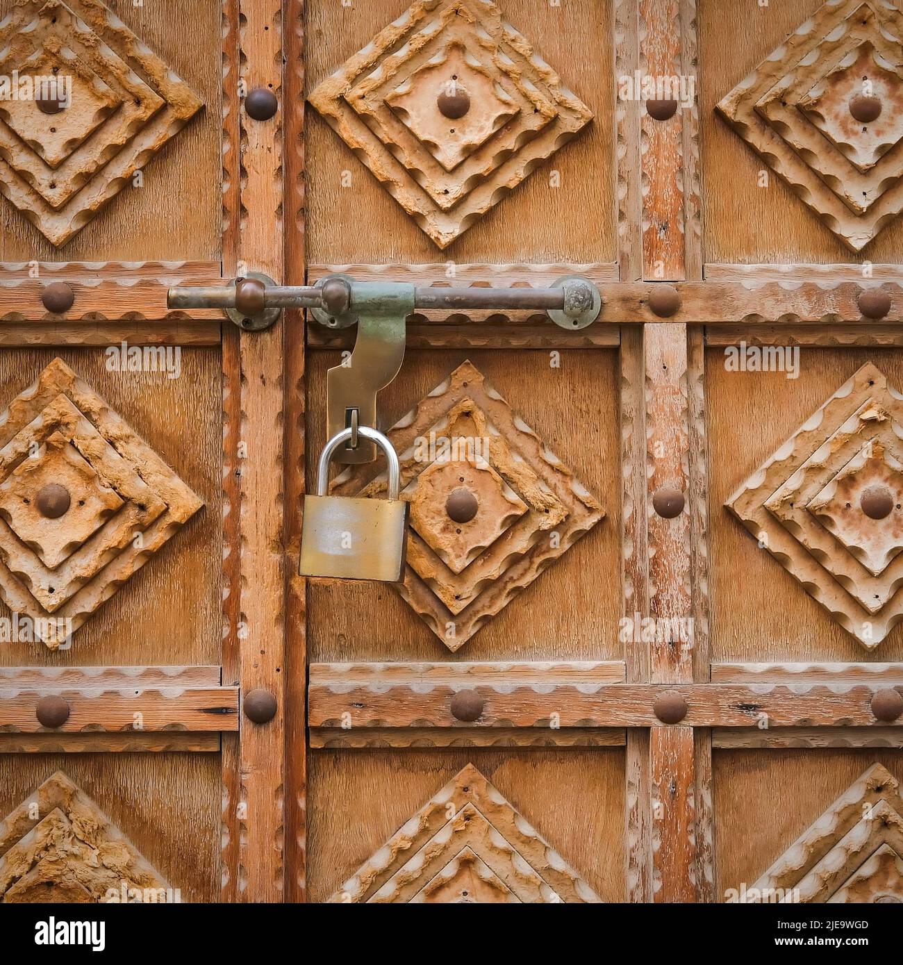 Fragment of minimalist wood carving design on antique timber gate. Vintage wooden entrance door with padlock Stock Photo