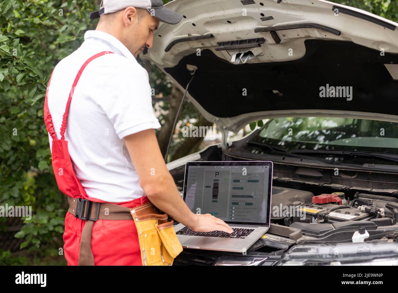 Mechanic with laptop near car engine. Modern car diagnostic program on