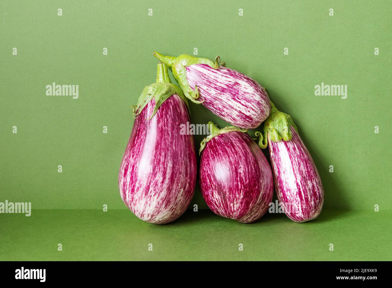 Three ripe eggplants with beautiful purple and pink striped patterns on green background. Natural organic farm vegetable food concept. Stock Photo