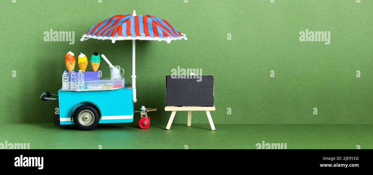 Mini shop Ice cream cart with blue red umbrella. Assortment of ice cream empty menu black chalkboard. Summer vacation concept. green background, copy Stock Photo
