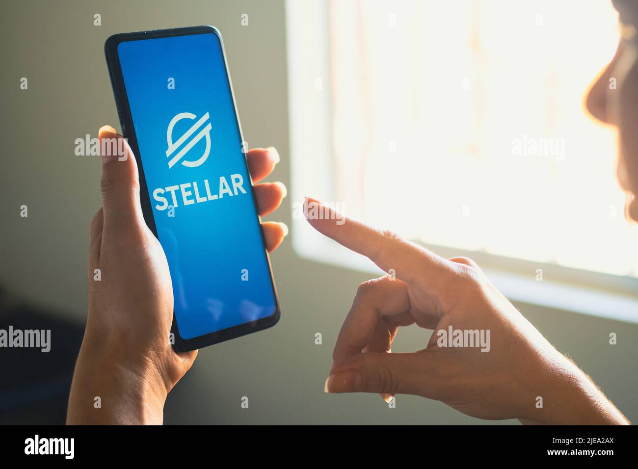 In this photo illustration, a woman holds a smartphone with the Stellar (XLM) logo displayed on the screen. Stock Photo