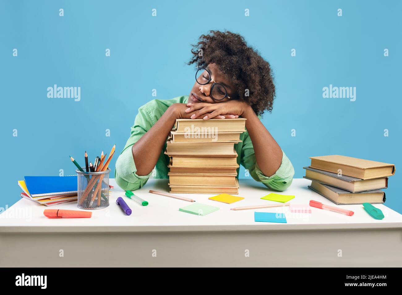 Exhausted black male student sleeping on desk on stacks of books, being tired while preparing for exam Stock Photo