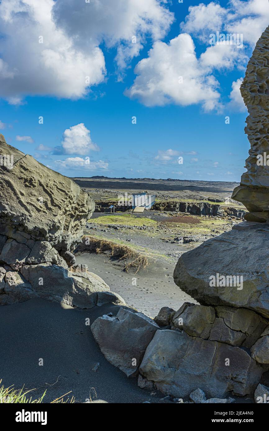 Landscape of Iceland on the Reykjanes peninsula. Rock face made of lava stones and black lava sand with blades of grass. Metal bridge over the Eurasia Stock Photo