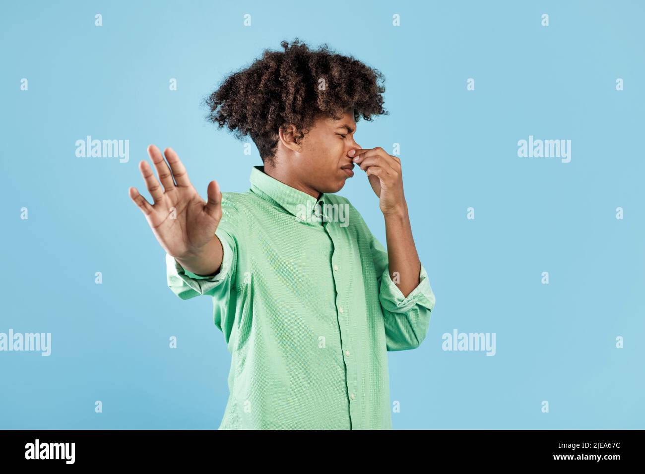 Terrible smell. African american guy closing his nose and gesturing STOP, feeling disgusted, blue background Stock Photo