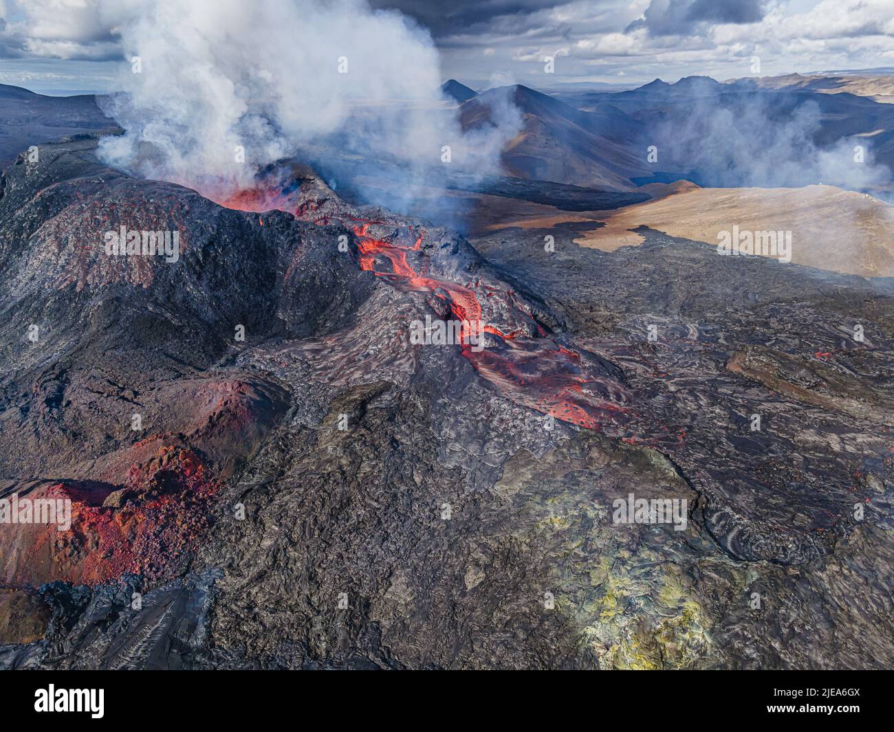 liquid magma flows from the volcanic crater. Volcano on Iceland's Reykjanes Peninsula. green, red gray and dark lava rocks around the crater. Steam an Stock Photo