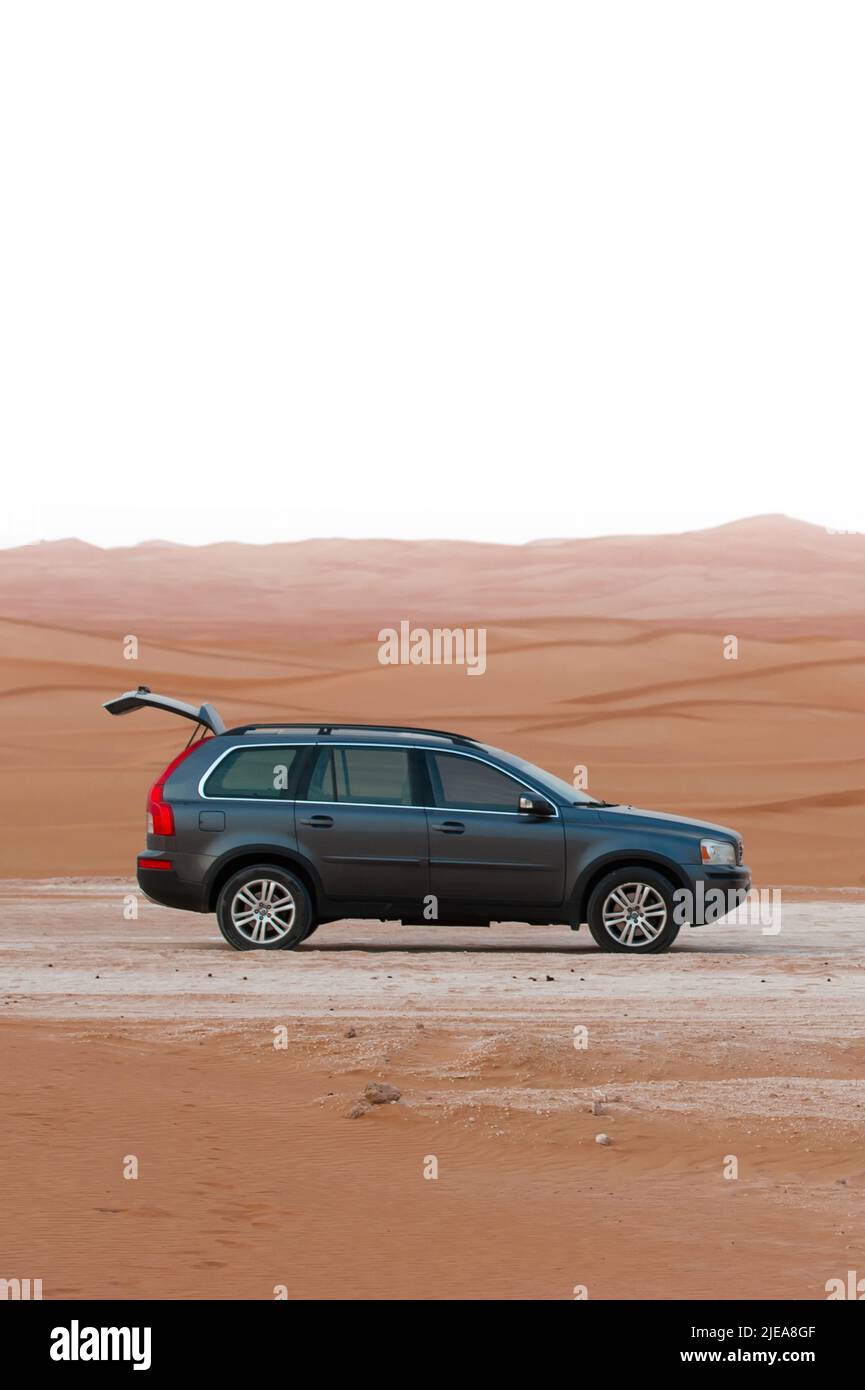 Dark gray Volvo XC90 SUV with open trunk parked on the road, in the middle of Al Wathba desert in Abu Dhabi, United Arab Emirates. Sand dunes behind. Stock Photo