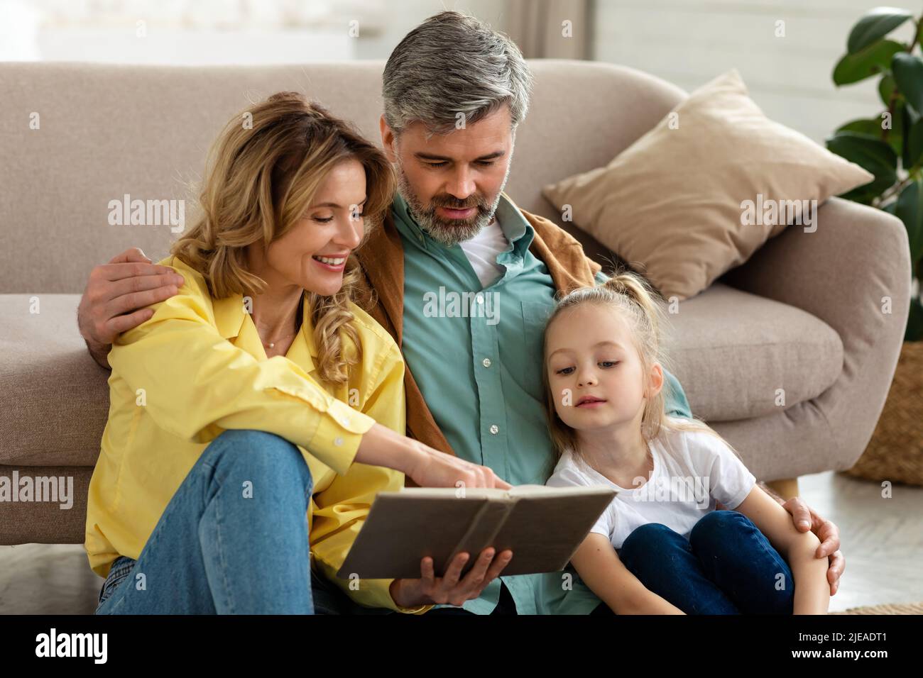 Happy Family Of Three Reading Book Spending Weekend At Home Stock Photo