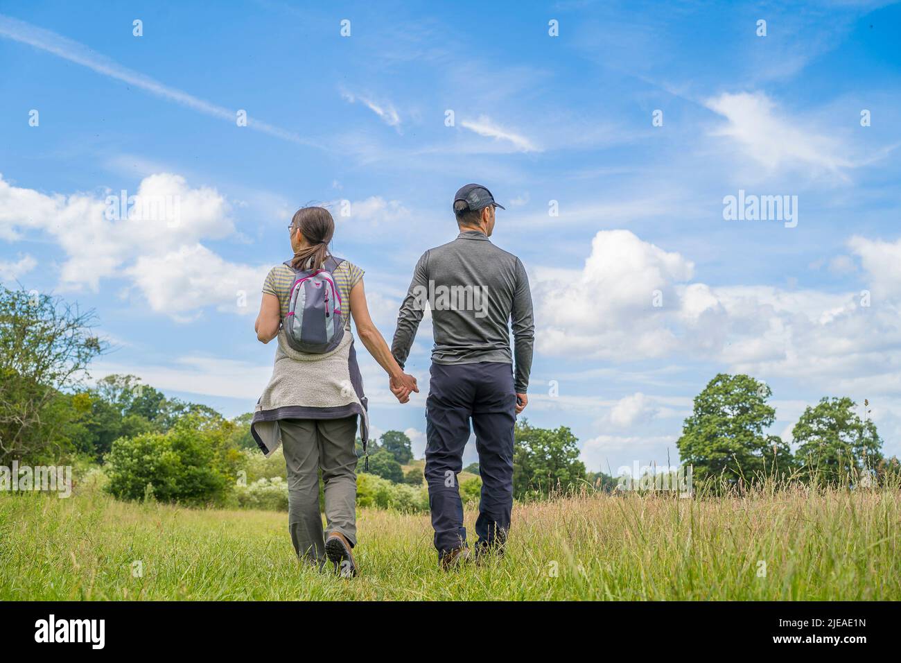 Kidderminster, UK. 26th June, 2022. UK weather: sunny weather and warm temperatures entice walkers for a stroll in the countryside. A couple, holding hands, enjoy a country walk through meadows admiring the natural world around them and the blue skies above. Credit: Lee Hudson/Alamy Live News Stock Photo