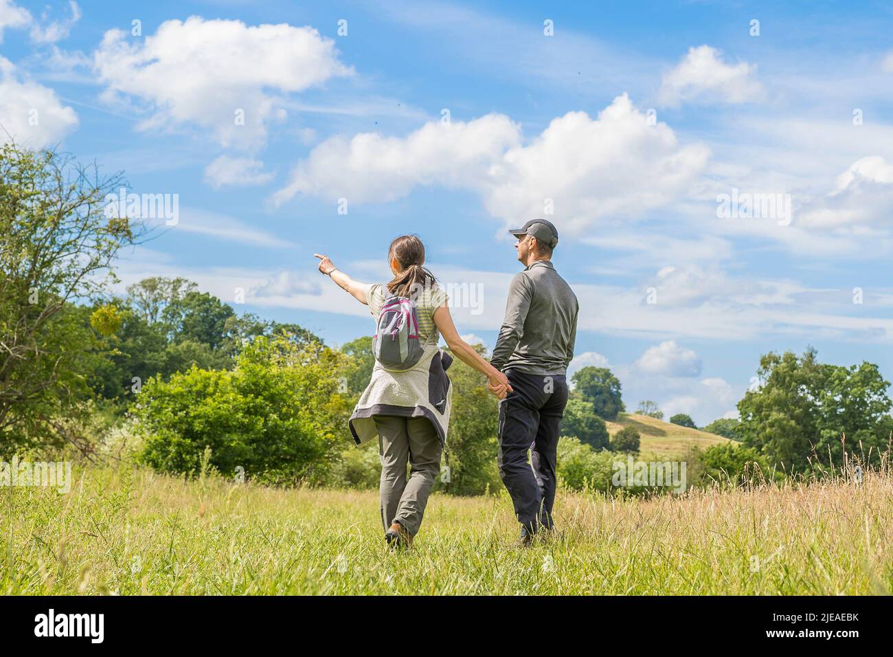 Kidderminster, UK. 26th June, 2022. UK weather: sunny weather and warm temperatures entice walkers for a stroll in the countryside. A couple holding hands walk through a country meadow enjoying the nature around them, with blue skies above. Credit: Lee Hudson/Alamy Live News Stock Photo