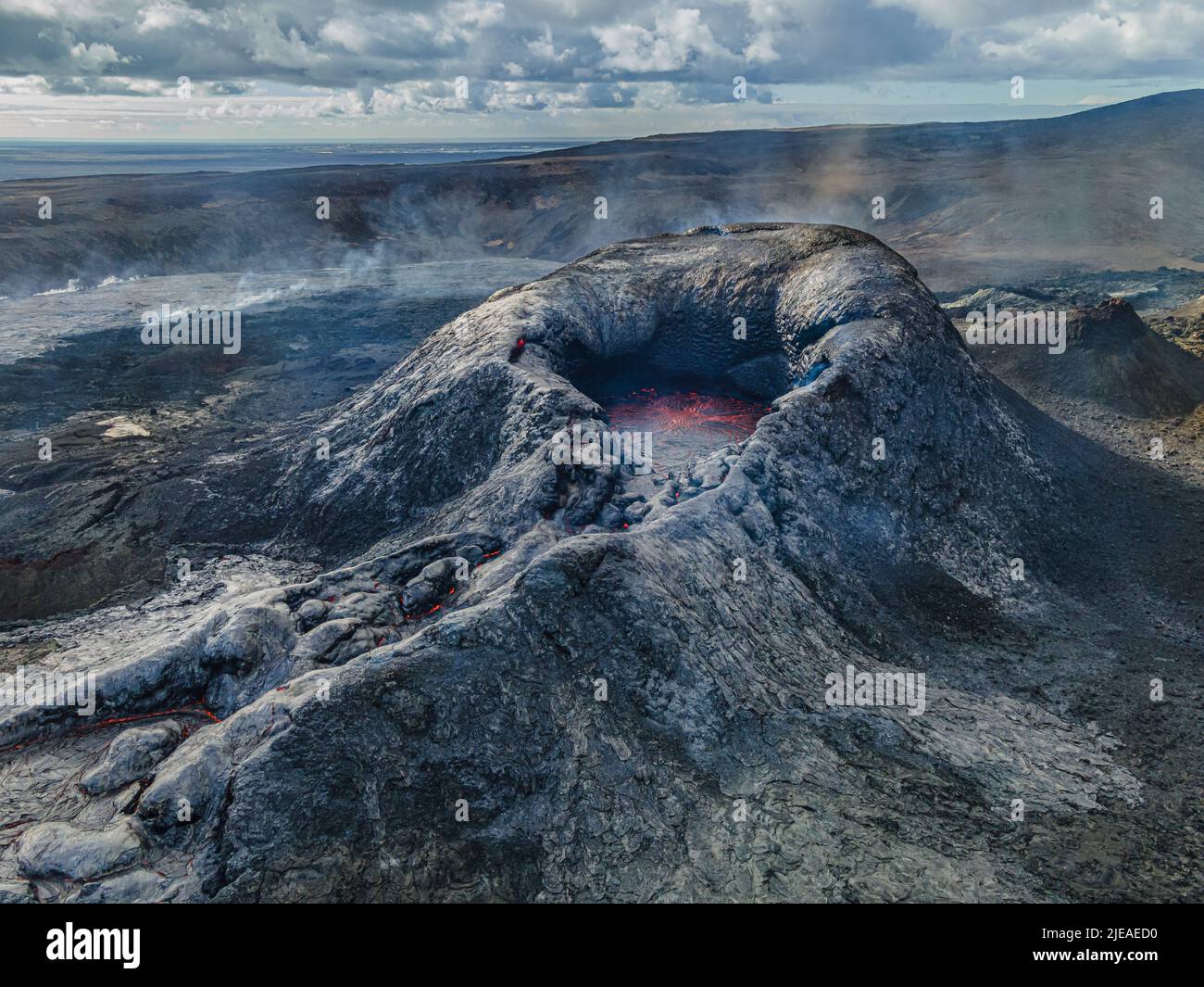 Landscape in Iceland. Volcanic crater on Reykjanes Peninsula by day. Crater before eruption. Dark cooled lava around the crater and steam. Dark rock a Stock Photo