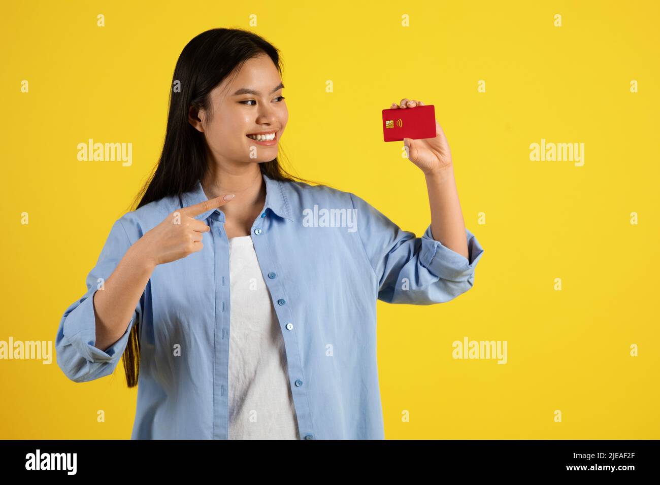 Cheerful happy young japanese female pointing finger at credit card, recommends save money Stock Photo