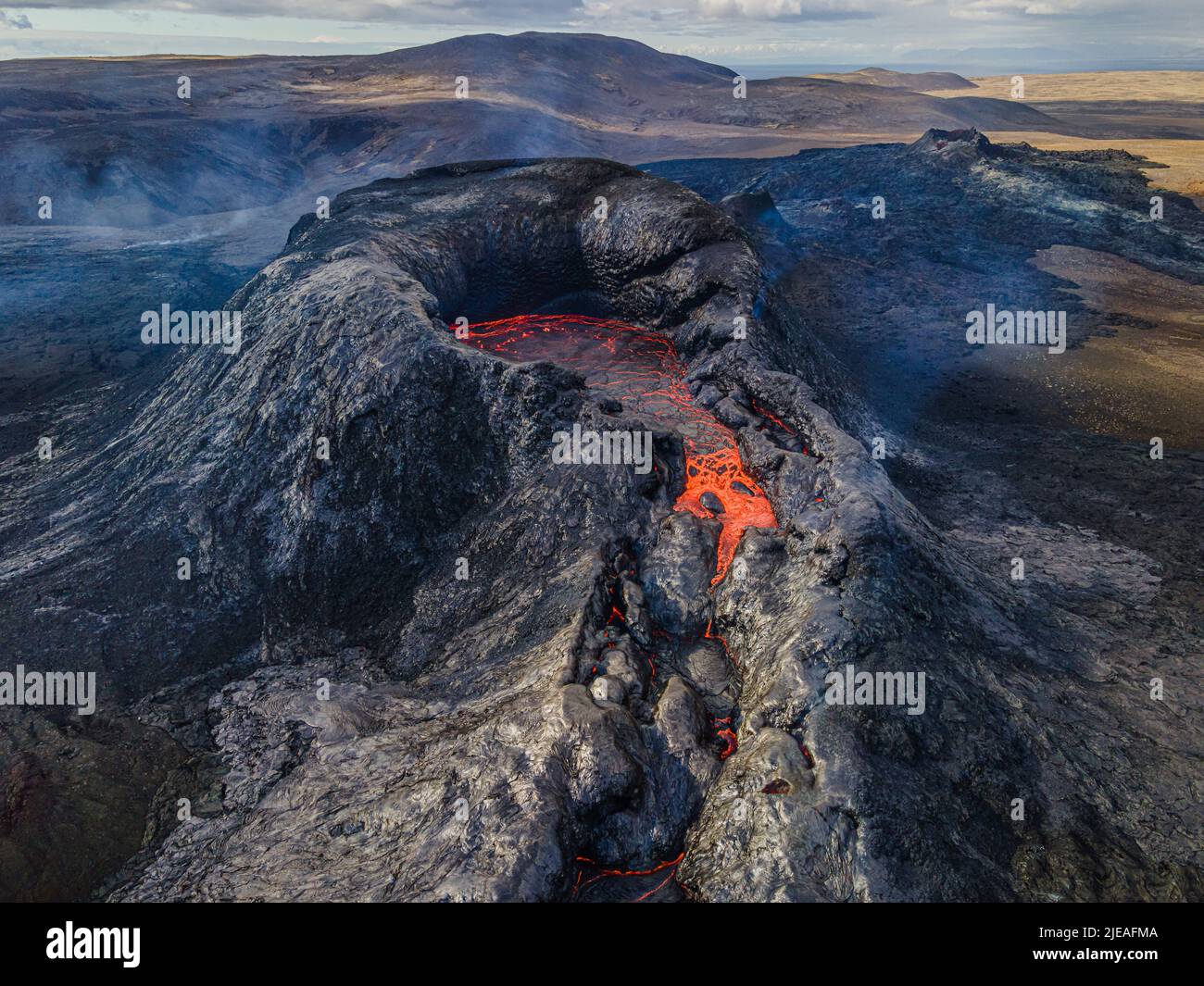 View into the crater of an active volcano with lava flow at the beginning of an eruption. Landscape on the Reykjanes Peninsula of Iceland. Puffs of sm Stock Photo