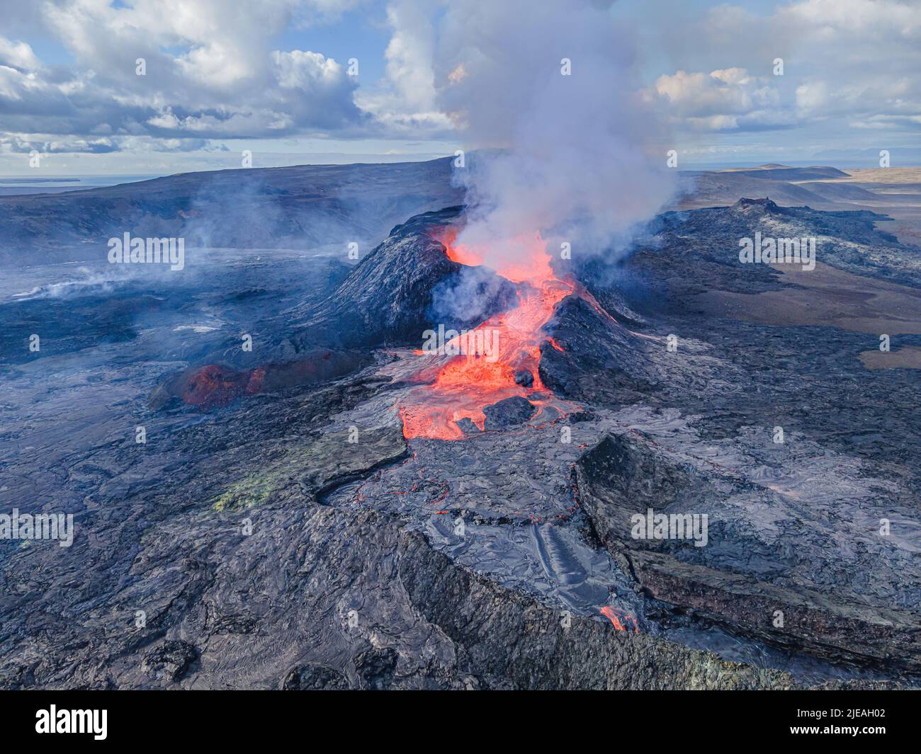 glowing hot lava pouring out of a volcano in Iceland. View into the crater of the Reykjanes Peninsula from above. Steam and smoke near the crater. Stock Photo