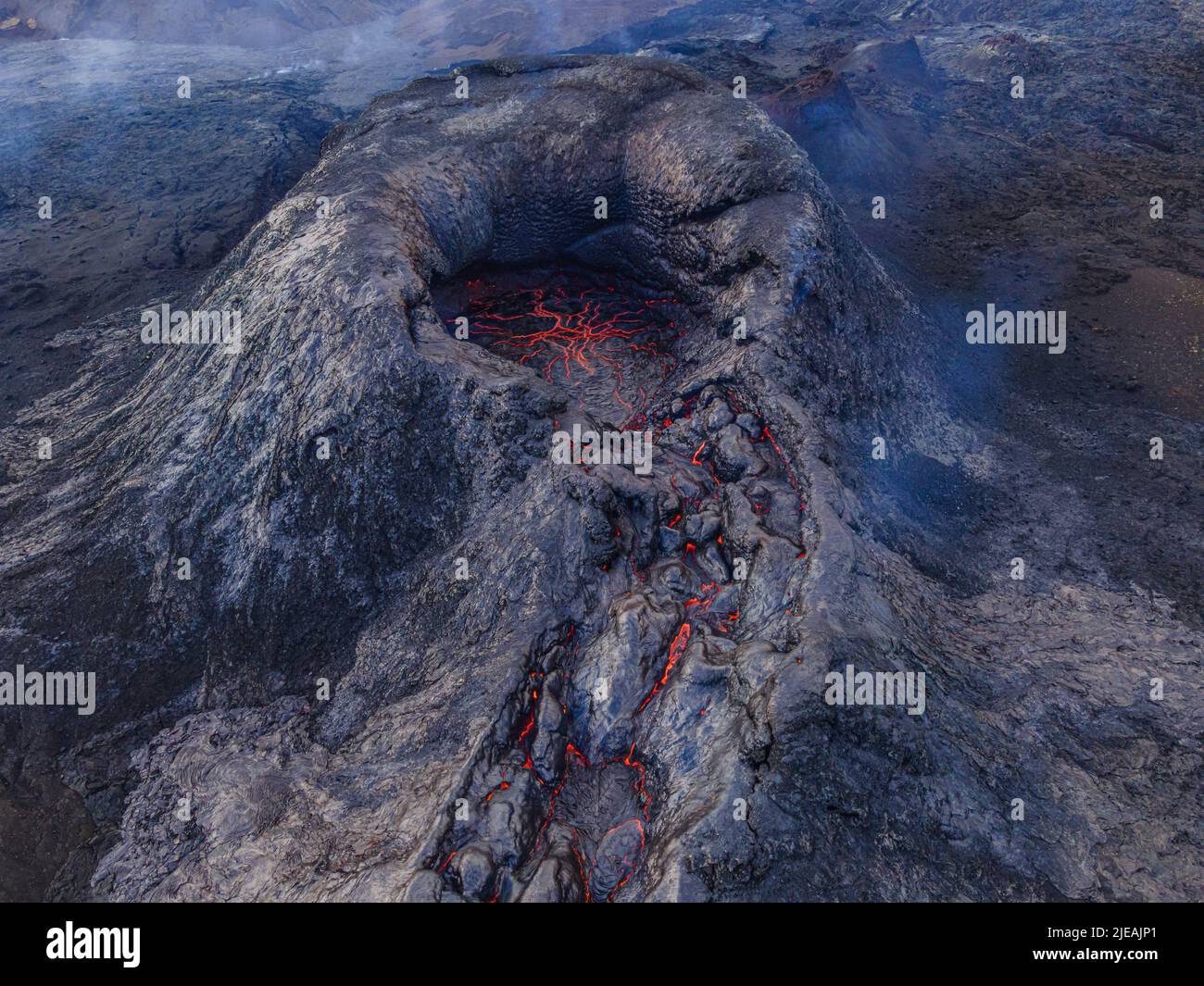 Volcano crater from above. View of the structures of red lava in the crater's mouth. Volcano just before eruption. dark, cooled magma rock around Stock Photo
