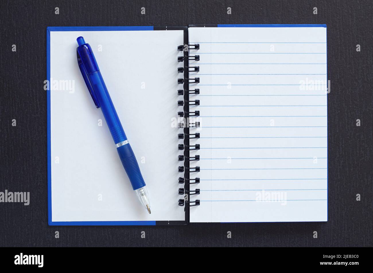 Notepad with a blue pen on black stone background, top view. Space for ...