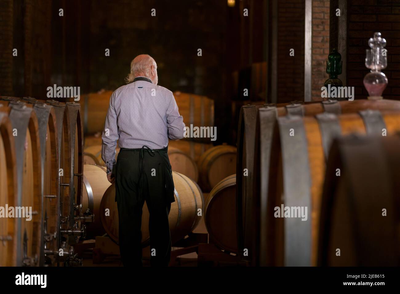 Senior man winemaker at winery checking barrels in wine cellar. Stock Photo
