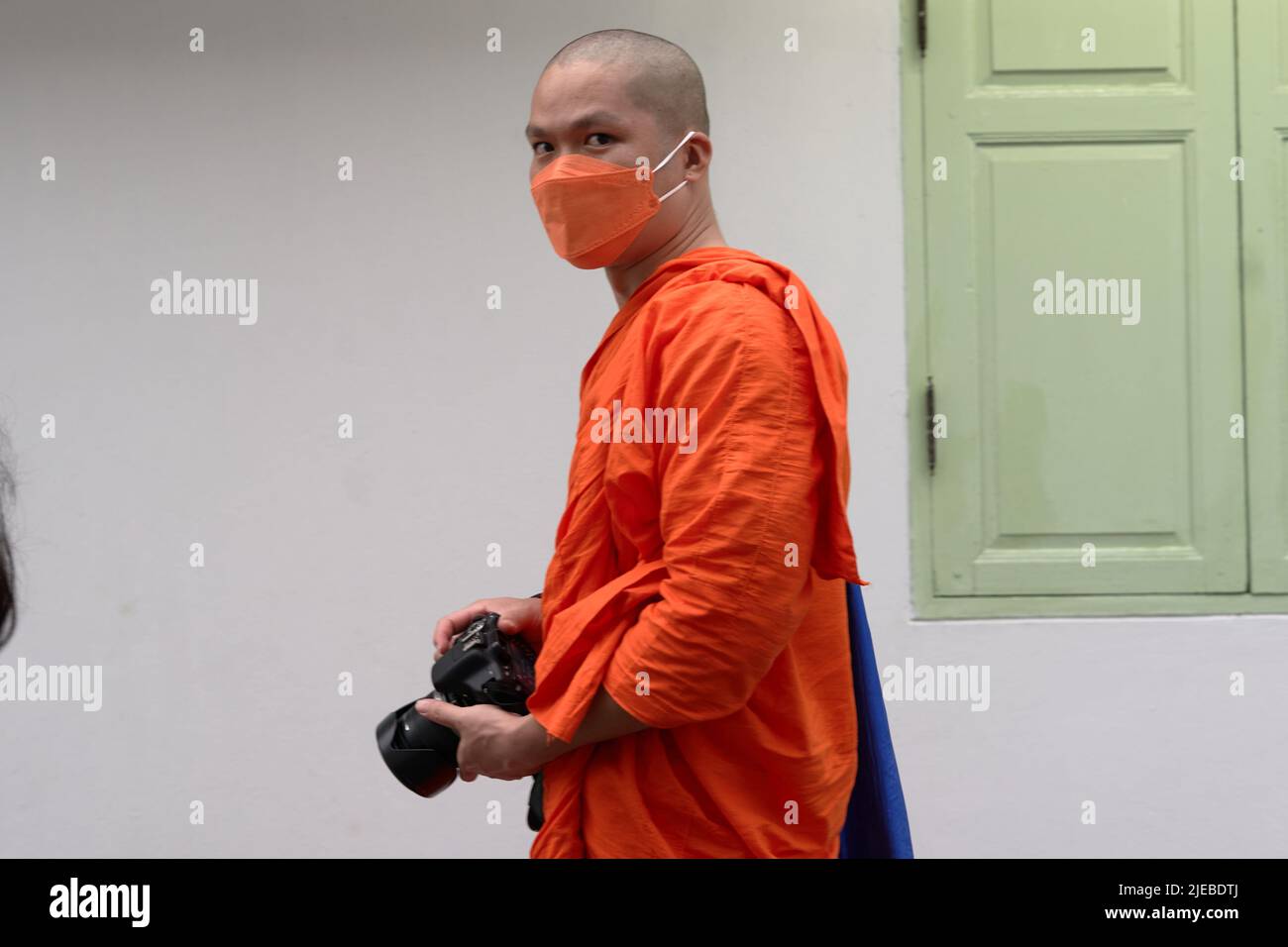 Buddhist monk with mask looking at the camera while walking holding a camera Stock Photo