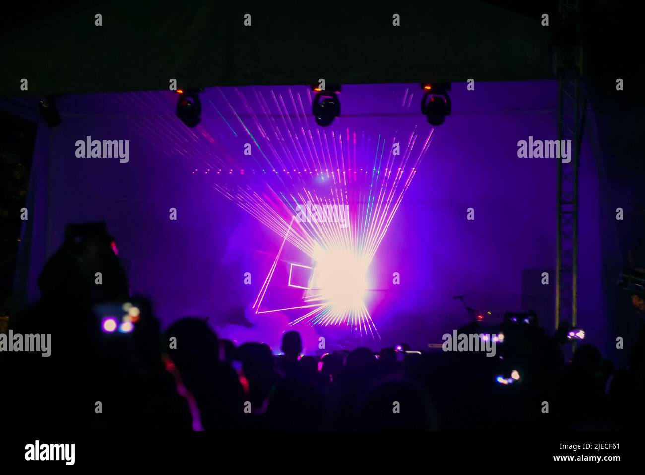 Purple laser neon beams. Crowd of people watching laser show at street festival. Many people enjoy the concert. Stock Photo