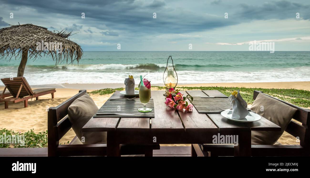 Restaurant or cafe on beach. Table setting with cocktail and flowers on sea background in tropical resort. Panoramic view of beautiful romantic dinner Stock Photo