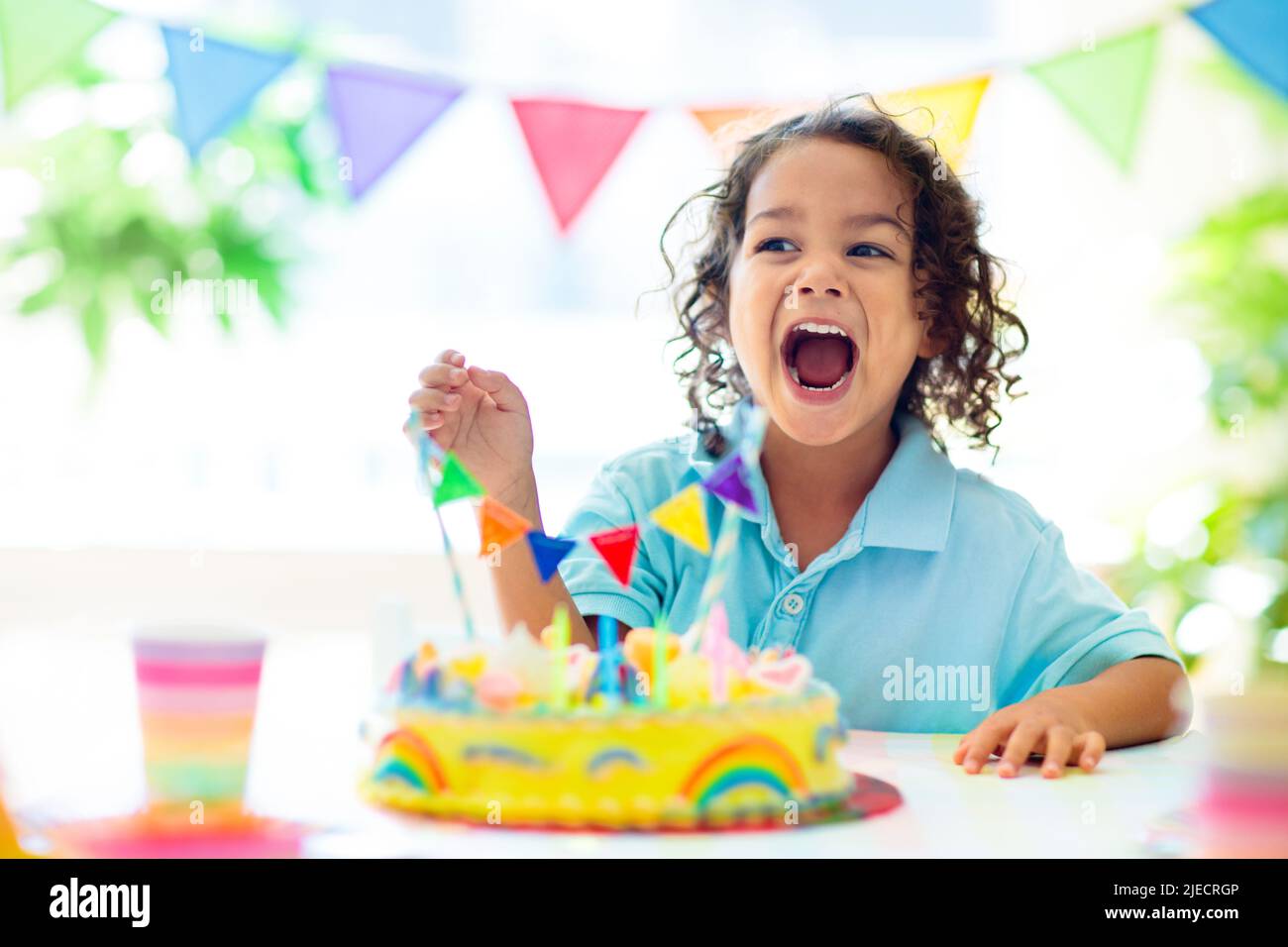 Kids birthday party. Children celebrate with colorful cake and gifts. Little curly boy blowing