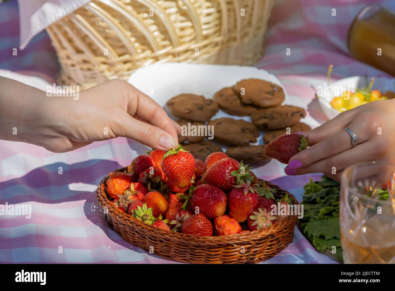 Close up of hands taking strawberries on a picnic in the park. Stock Photo