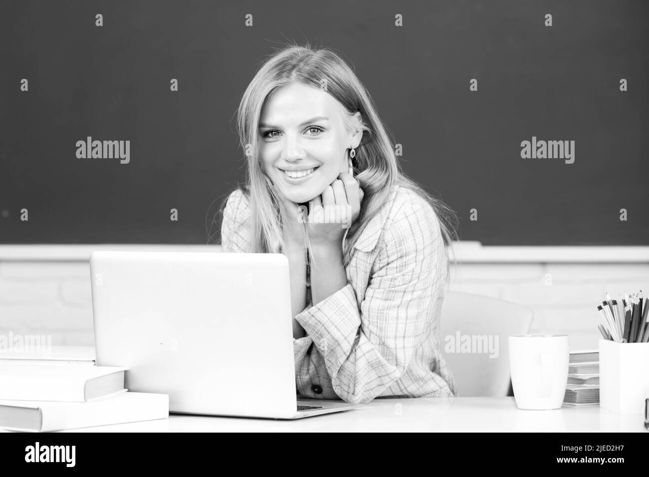Portrait of smiling young college student studying in classroom. Creative young smiling female student using laptop. Stock Photo
