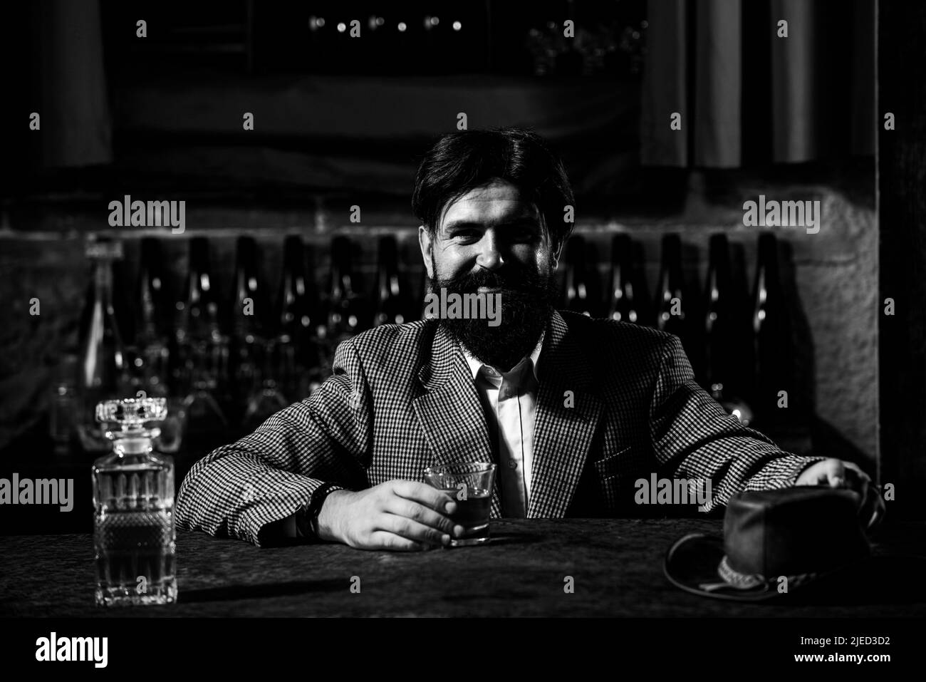 Vintage worker man with long beard holding whiskey. Sitting in bar. Stock Photo