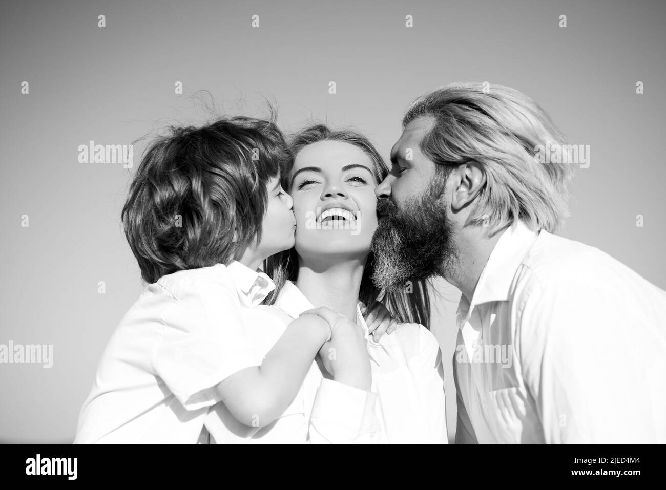 Mothers day. Parenting. Happy family. Motherhood fatherhood. Son and dad kiss mother. Young family with child. Kids love. Stock Photo