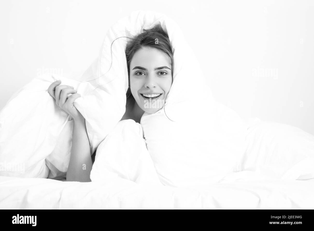 Funny woman with beautiful face is sitting on the bed, wrapped in soft